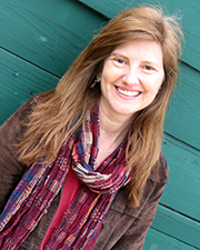A person smiling at the camera, wearing a multicolored scarf and standing in front of a green wooden background.