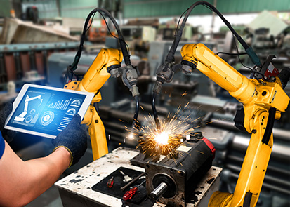 Two robot arms being controlled by a person with a tablet in an engineering facility