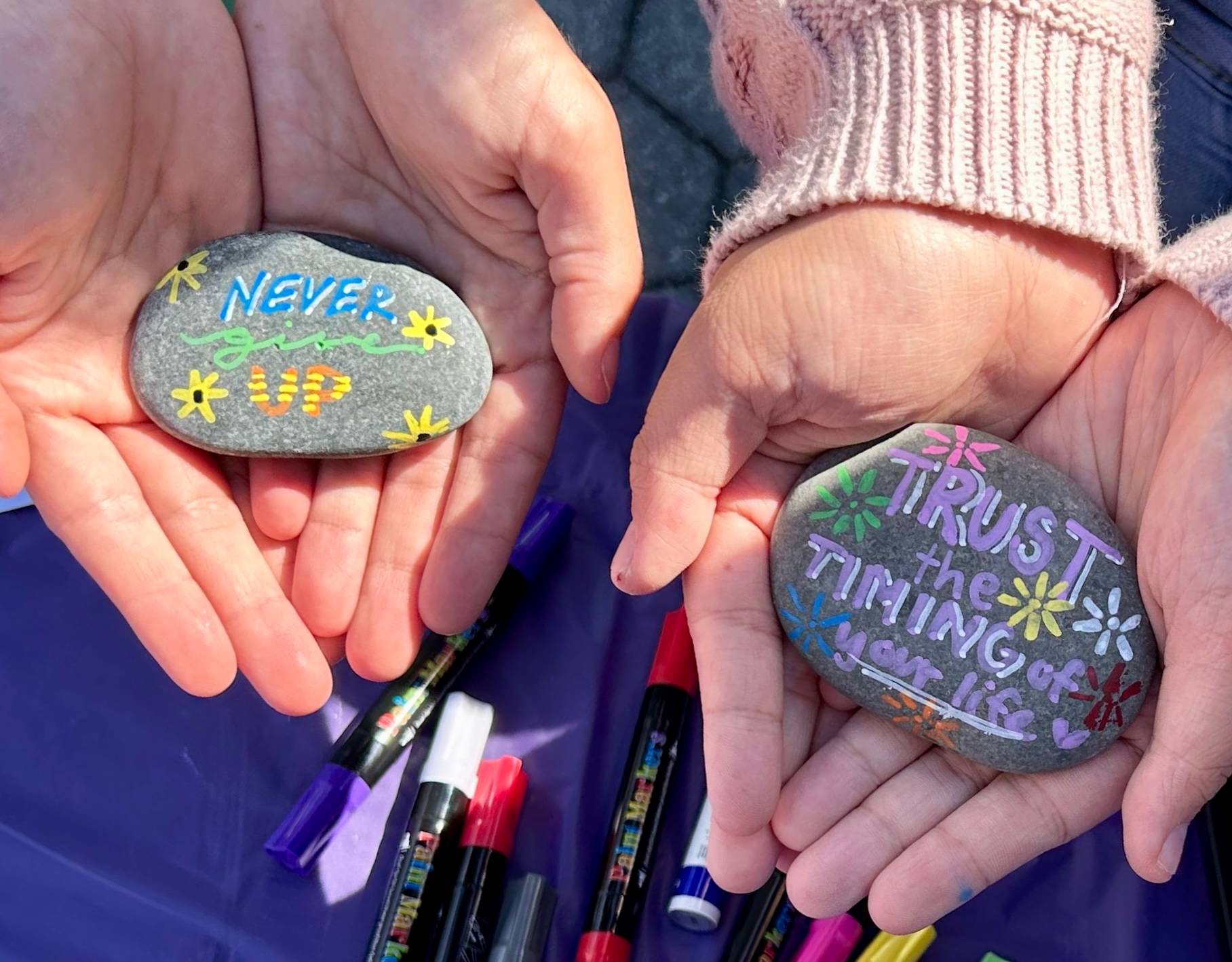 Image of two students holding rocks of hope they painted with the words "Never Give Up" and "Trust the Timing of your Life"