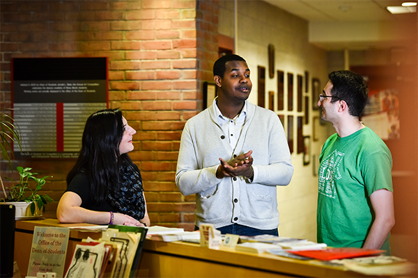 Two graduate students give an explanation to an undergraduate student in a campus office